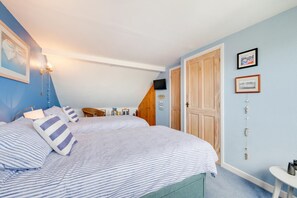 Ein Schlafzimmer mit zwei Betten, einem Sessel, einem kleinen Tisch und einem Fernseher an der Wand.