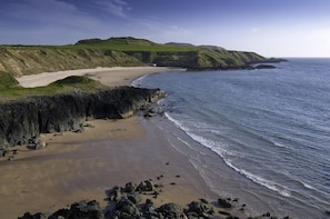 A coastal landscape with a sandy beach, rocky cliffs, and green hills. - 3 Bed in Aberdaron (oc-23321) (Aberdaron)