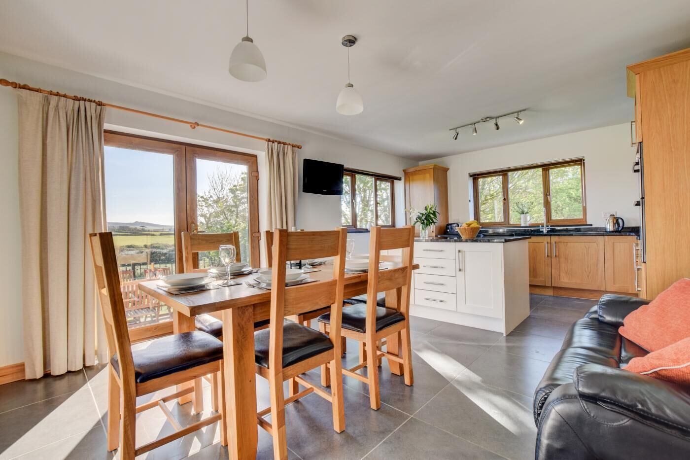 A modern kitchen with wooden cabinets, a dining area with a table and chairs, and a living area with a sofa.