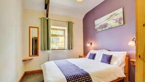 Una camera da letto con un letto, una finestra con tende, un quadro appeso al muro e una porta in legno.