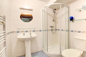 Een badkamer met een douche met glazen wand, een wastafel op een zuil en een toilet.
