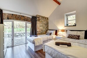 Quarto com duas camas, parede de pedra, janela e vista para o exterior.