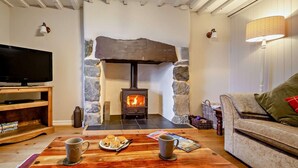 A cozy living room with a stone fireplace, a flat-screen TV, a wooden coffee table with mugs and snacks, and a comfortable sofa. - 4 Bed in Caernarfon (oc-30479) (Dinas)