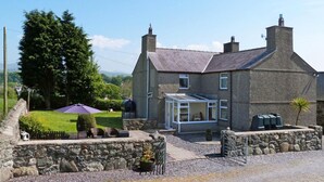 A stone house with a conservatory, a garden, and a stone wall. - 4 Bed in Caernarfon (oc-30479) (Dinas)