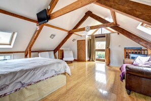A spacious attic bedroom with a sloped ceiling, wooden beams, a large bed, a leather sofa, and a view through a window. - 2 Bed in Llandysul (oc-23391) (Ffostrasol)