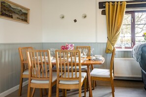 Una sala da pranzo con tavolo apparecchiato per quattro persone, sedie di legno, un quadro appeso e una finestra con tende.
