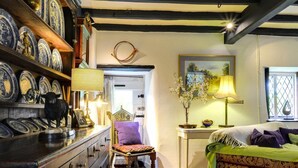 Une pièce avec un parquet en chevrons, un lit recouvert d’une literie à motifs, une commode en bois dotée de tiroirs et une étagère ornée d’assiettes bleues et blanches.