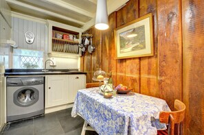 Pieni, käytännöllinen keittiö, jossa on pyykinpesukone, puupanelointi, kello ja kehystetty taulu.