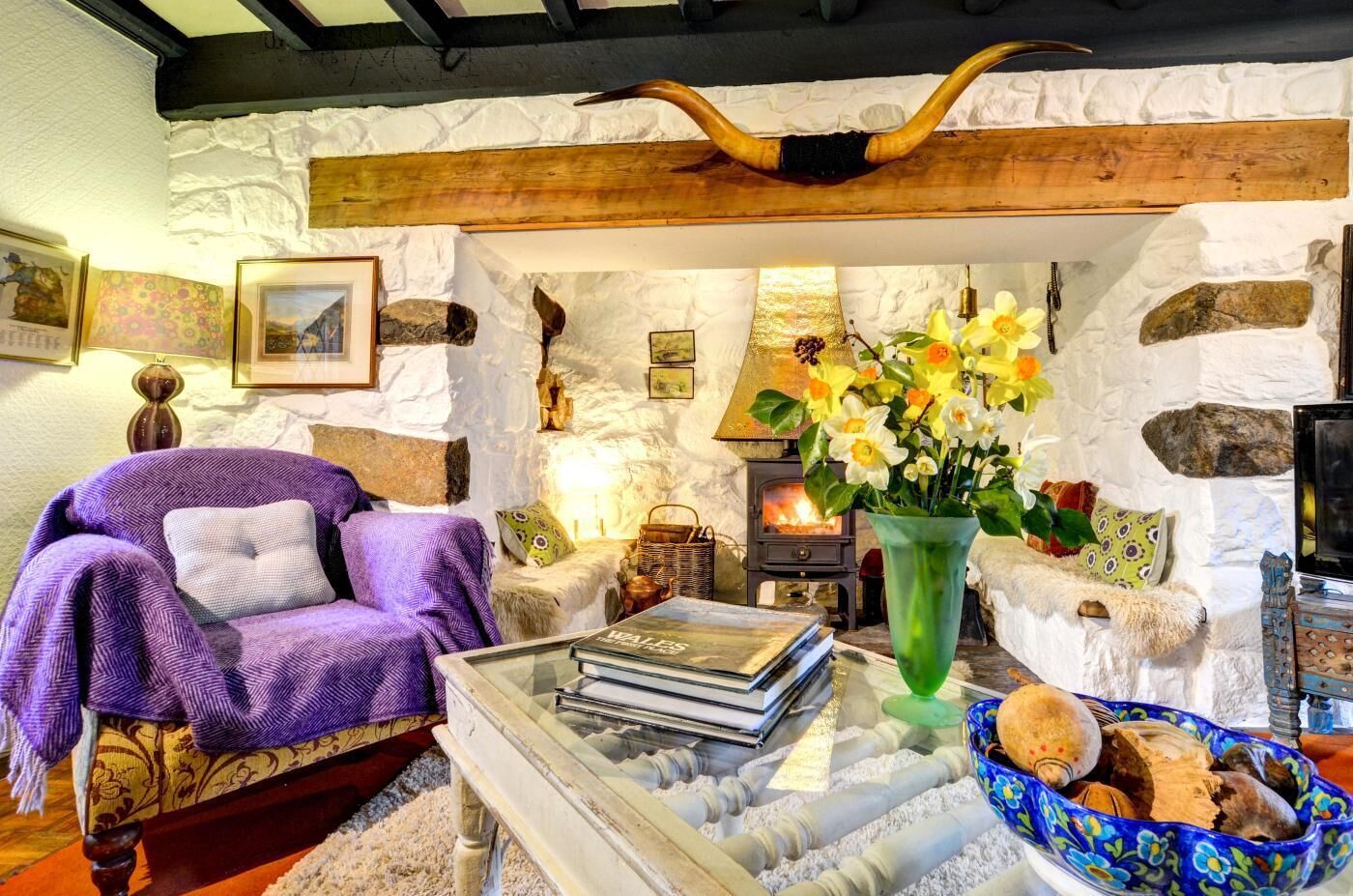 A cozy living room with a stone wall, a fireplace, a purple sofa, a glass coffee table, and a vase with flowers.