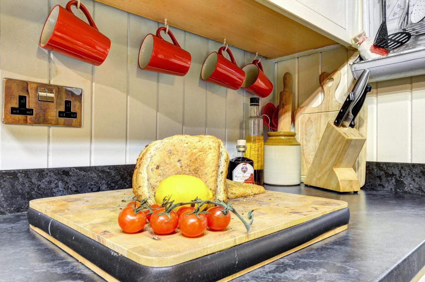 A kitchen counter with a cutting board, bread, tomatoes, and a bottle of honey mustard.