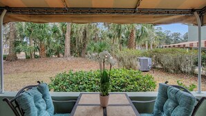 A covered outdoor seating area with a table and chairs, surrounded by lush greenery and palm trees. - Evian 157- 2BR/2BA Pool & Tennis Courts (Hilton Head Island)