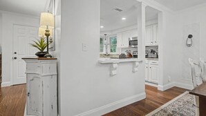 A modern kitchen with white cabinetry, a central island, and a dining area with a wooden table. - Evian 157- 2BR/2BA Pool & Tennis Courts (Hilton Head Island)