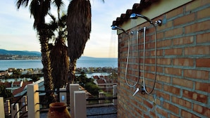 A brick wall with a showerhead and hose, a large terracotta pot, and a view of a coastal town and sea. - Discover your exclusive oasis in Ganzirri: the villa overlooking the Strait (Messina)