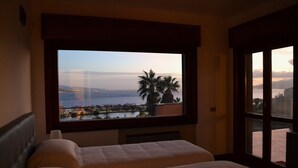 A hotel room with a large window overlooking a body of water and a cityscape. - Discover your exclusive oasis in Ganzirri: the villa overlooking the Strait (Messina)