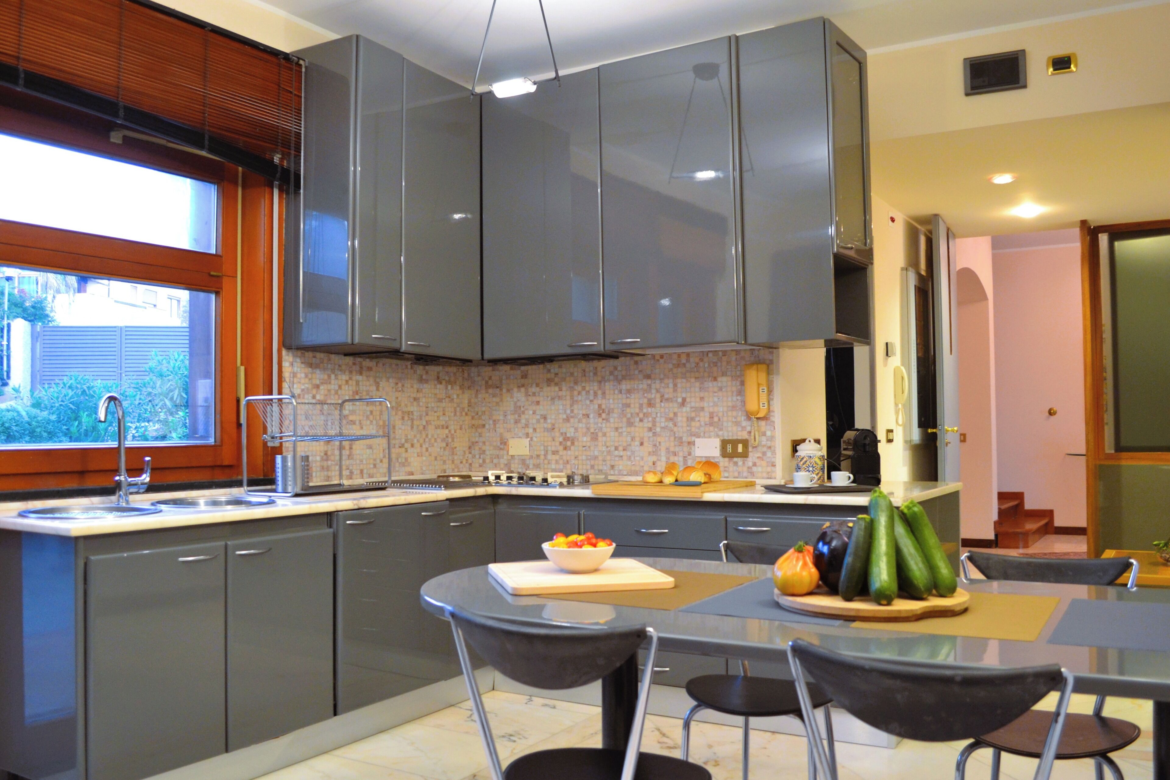 A modern kitchen with grey cabinets, a dining area with a table and chairs, and a view of the outdoors through a window.