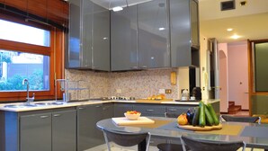 A modern kitchen with grey cabinets, a dining area with a table and chairs, and a view of the outdoors through a window. - Discover your exclusive oasis in Ganzirri: the villa overlooking the Strait (Messina)