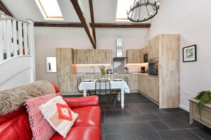 Eine moderne Küche mit Holzschränken, einem Esstisch und einer roten Ledersofa mit einem gemusterten Zierkissen.
