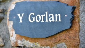 Une plaque de pierre portant l’inscription « Y Goran » est fixée à un mur de pierre érodé par les intempéries.