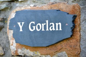 Une plaque de pierre portant l’inscription « Y Goran » est fixée à un mur de pierre érodé par les intempéries.