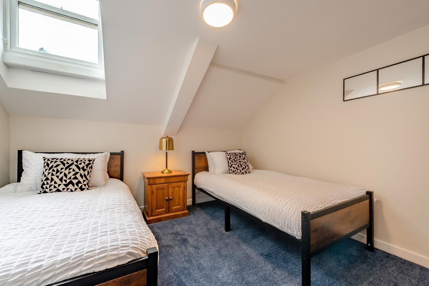 Une chambre avec deux lits simples, une table de chevet, une lampe, un luminaire au plafond et une fenêtre.