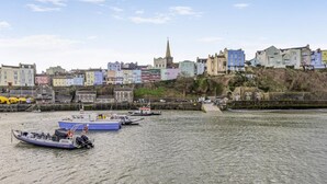 Un pueblo costero con edificios coloridos, una imponente torre de iglesia y barcos amarrados a lo largo del malecón.