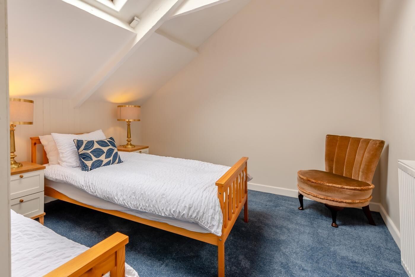 Een slaapkamer met een bed, een stoel, een nachtkastje en een lamp.