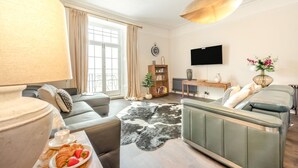 A living room with a sofa, a coffee table with pastries, a TV, and a bookshelf. - 2 Bed in Tenby (oc-25953) (Tenby)