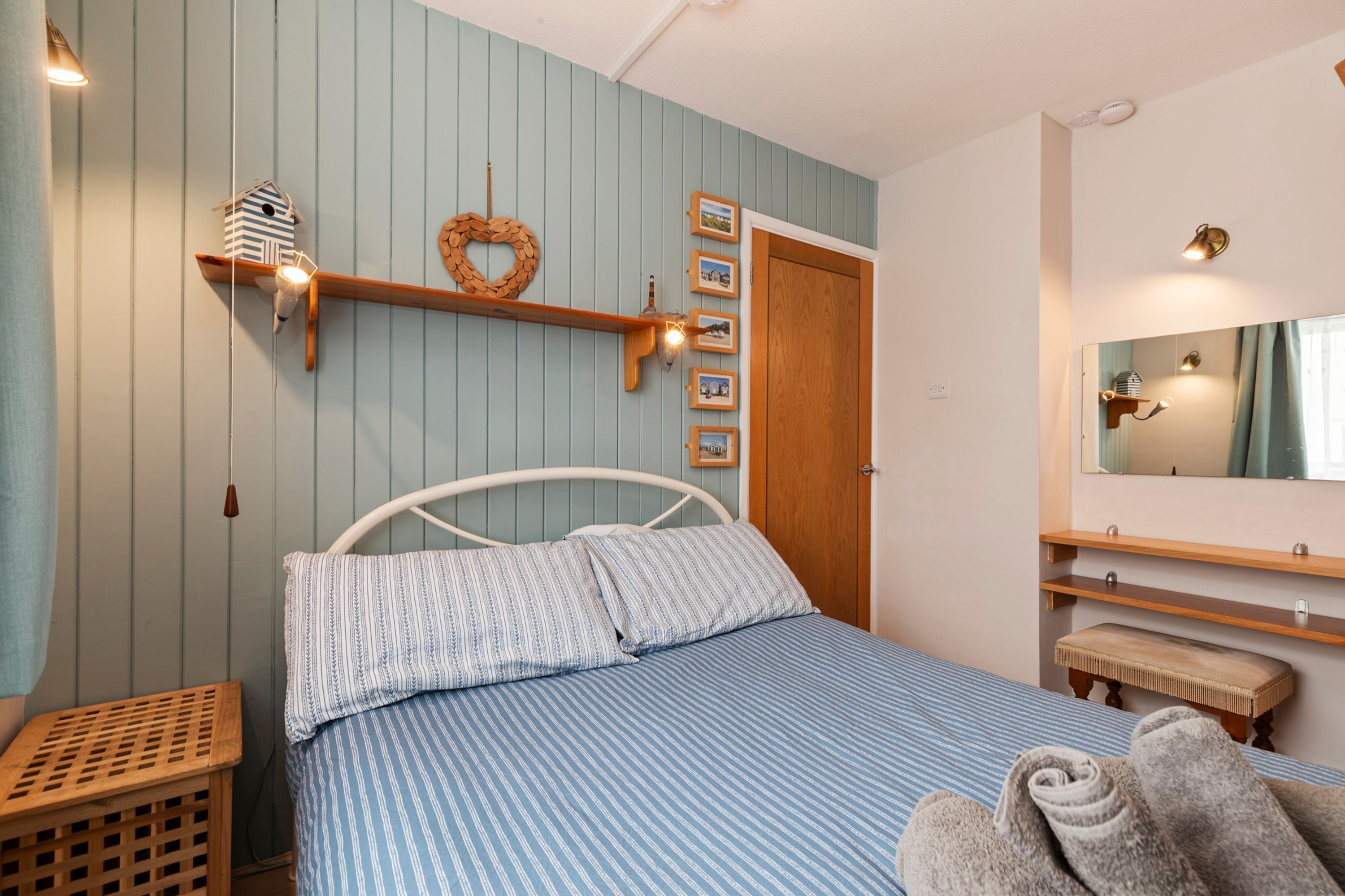 Een slaapkamer met een bed, een houten bankje, een wandplank met foto’s, een houten deur en een spiegel.