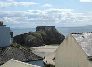 Blick auf die Küste mit einer markanten Felsformation, einem Gebäude darauf und einem Strand im Vordergrund.