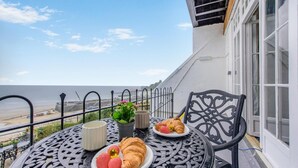 Balcón con mesa dispuesta para el desayuno, incluyendo cruasanes y fresas, con vistas a una playa.