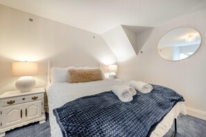 Een slaapkamer met een bed, twee nachtkastjes, een ronde spiegel en een plafondlamp.