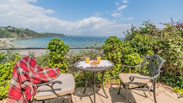 Terraço com duas cadeiras e uma mesa, com vista para a costa, barcos e praia.
