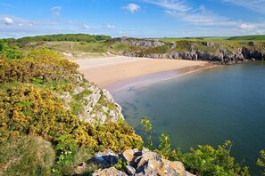 A coastal landscape with a sandy beach, rocky cliffs, and green hills. - 1 Bed in Tenby (oc-25957) (Tenby)