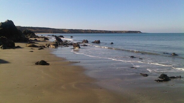 Une plage avec un ciel dégagé, des affleurements rocheux et des vagues calmes.