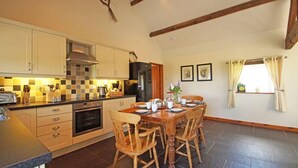 A kitchen with a dining table and chairs, a stove, oven, and a refrigerator. - 9 Bed in Pwllheli (oc-387040) (Pwllheli)