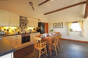 A kitchen with a dining table and chairs, a stove, oven, and a refrigerator. - 9 Bed in Pwllheli (oc-387040) (Pwllheli)