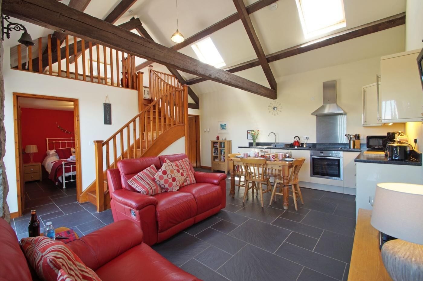 A spacious living area with a red leather sofa, a wooden dining table, and a kitchen with modern appliances.