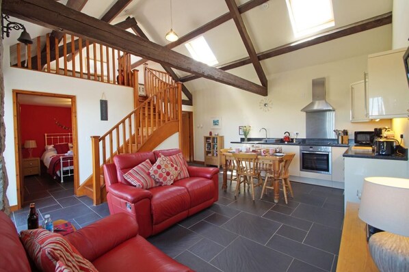 A spacious living area with a red leather sofa, a wooden dining table, and a kitchen with modern appliances. - 9 Bed in Pwllheli (oc-387040) (Pwllheli)