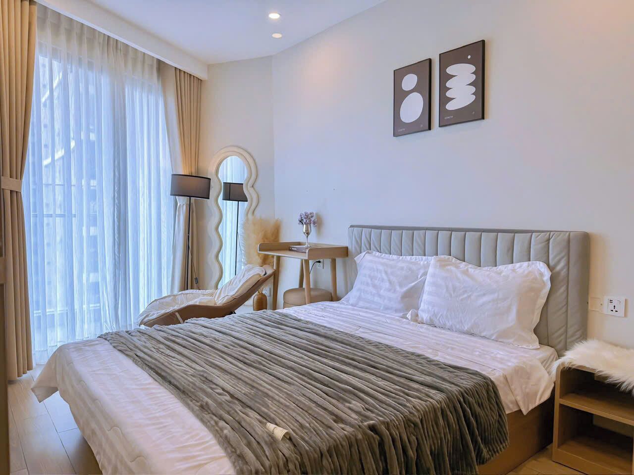 A hotel room with a large bed, a chair, a small table, and artwork on the wall.