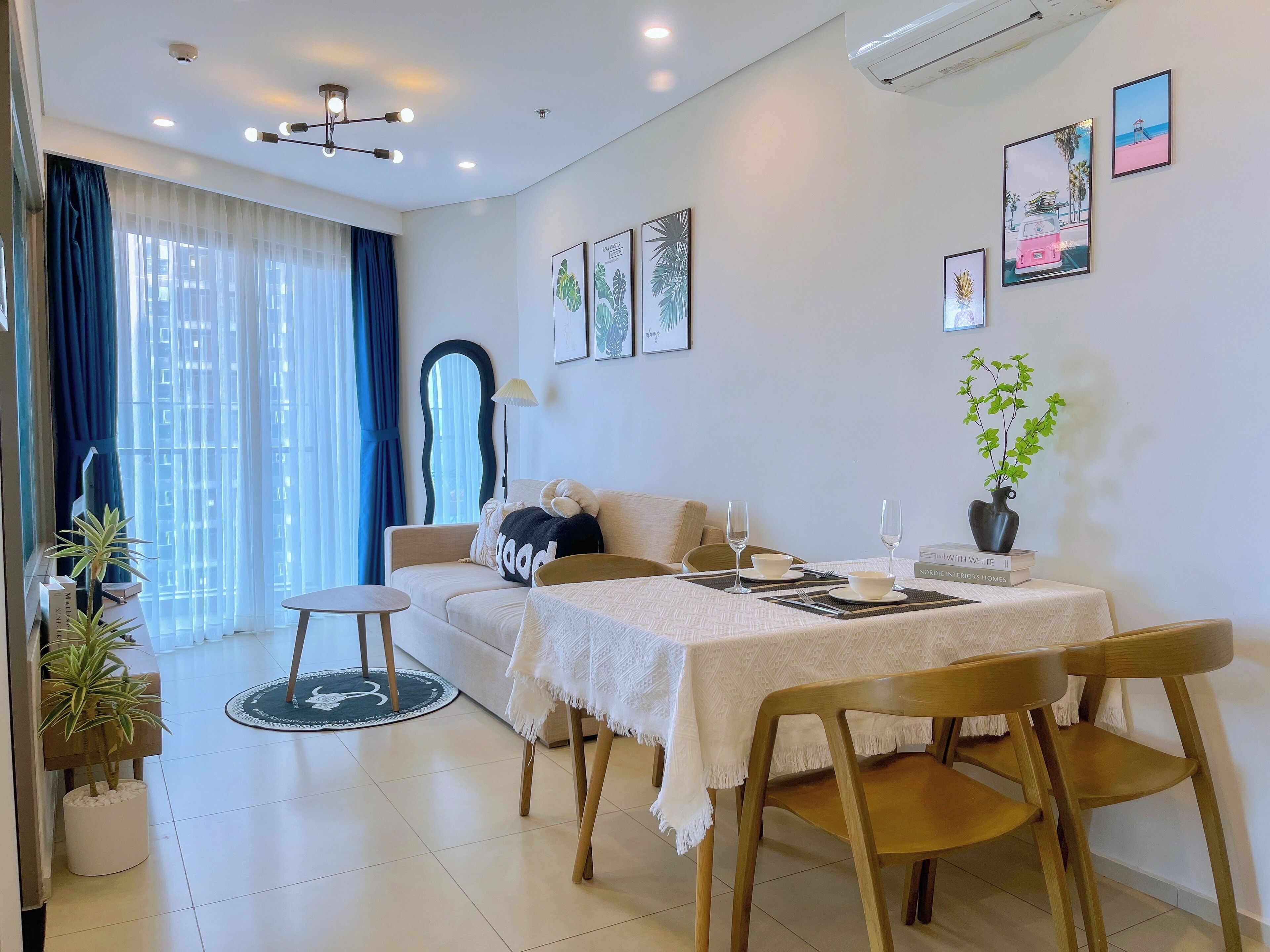 A modern living room with a sofa, dining table, chairs, and a large window with curtains.
