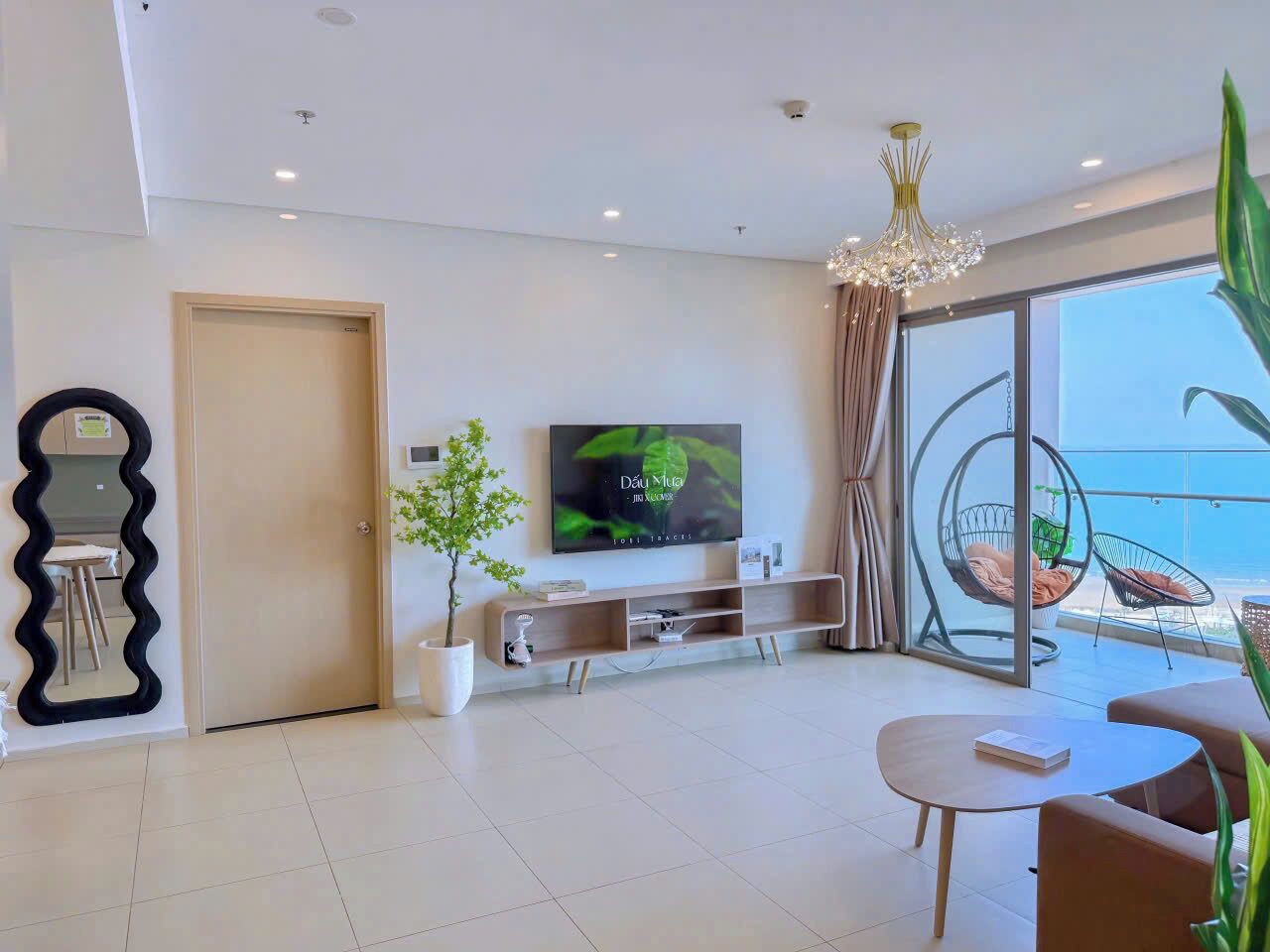 A modern living room with a TV, a dining table, a plant, and a balcony with a view.