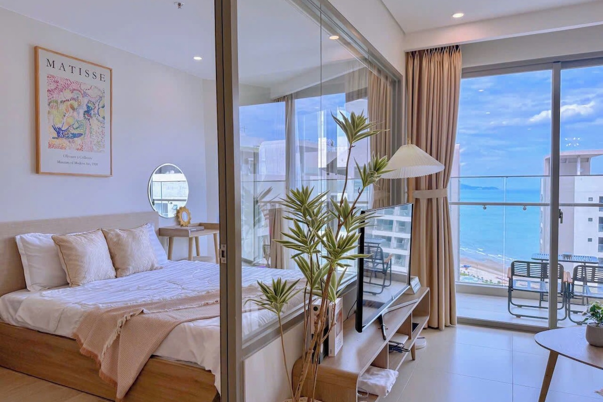 Habitación de hotel moderna con una cama, televisión, balcón con vistas al mar y un cuadro en la pared.