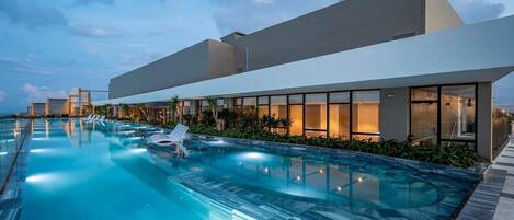 Un hôtel moderne doté d’une grande piscine, de chaises longues et d’une façade bien éclairée.