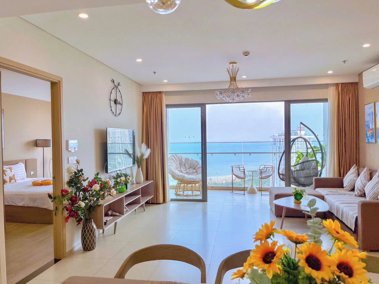 Una sala de estar moderna con sofá, mesa de centro y comedor. Hay un balcón con vista al mar.