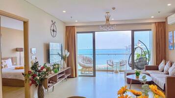 A modern living room with a sofa, coffee table, and a dining area. There is a balcony with a view of the sea.