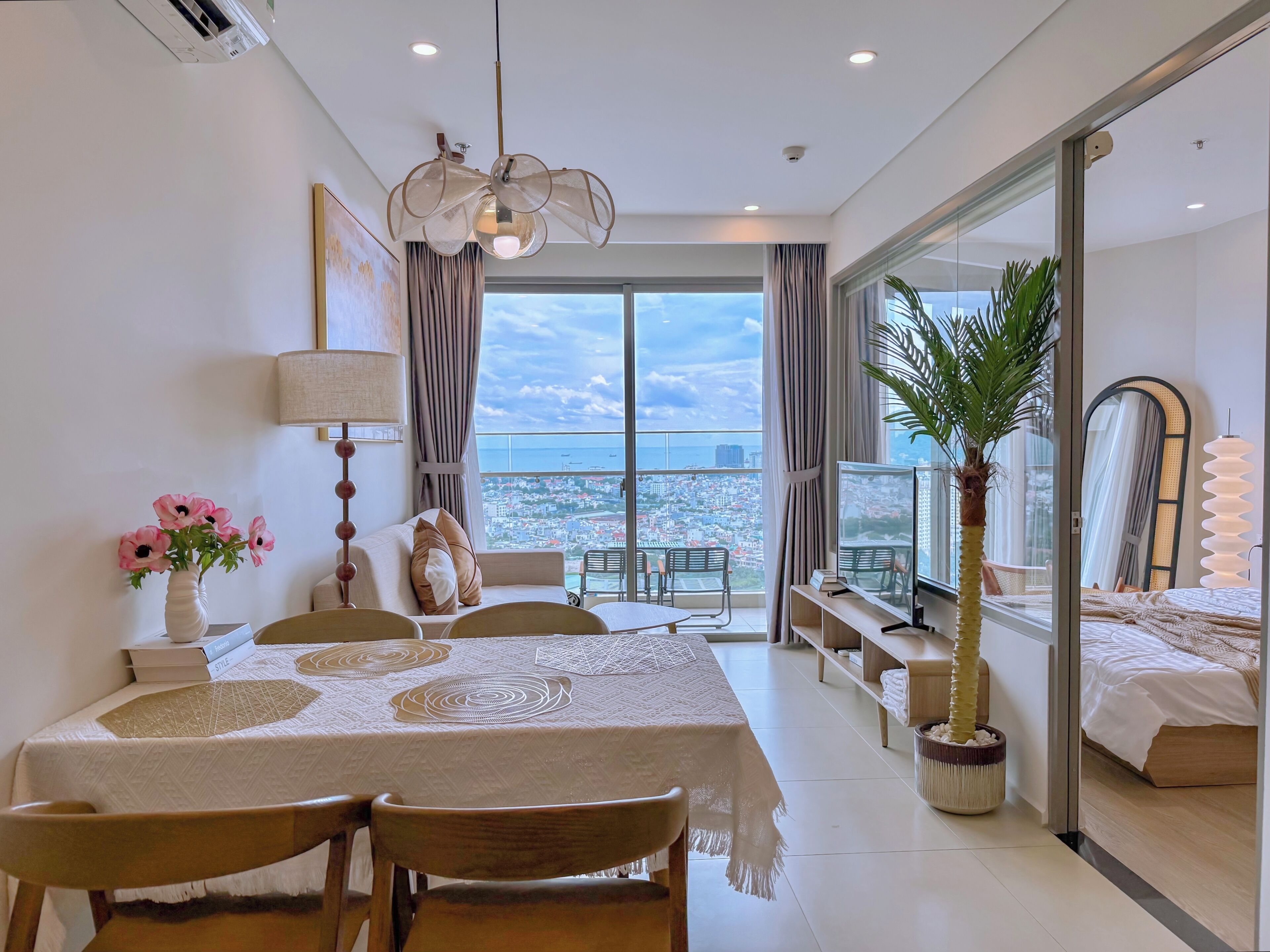A modern hotel room with a balcony, a dining area, and a large window offering a city view.