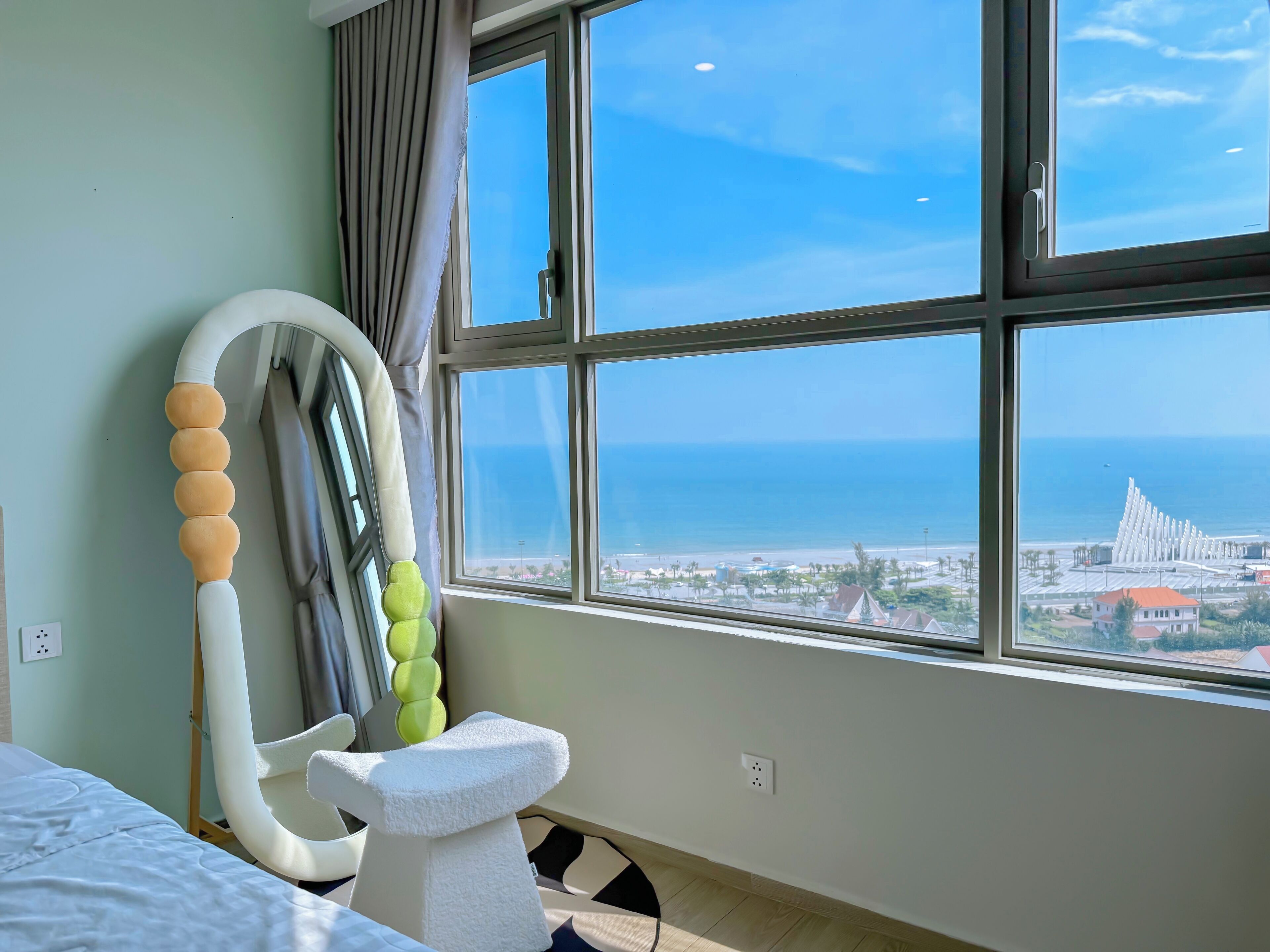 A hotel room with a large window offering a view of the sea and a distant cityscape.
