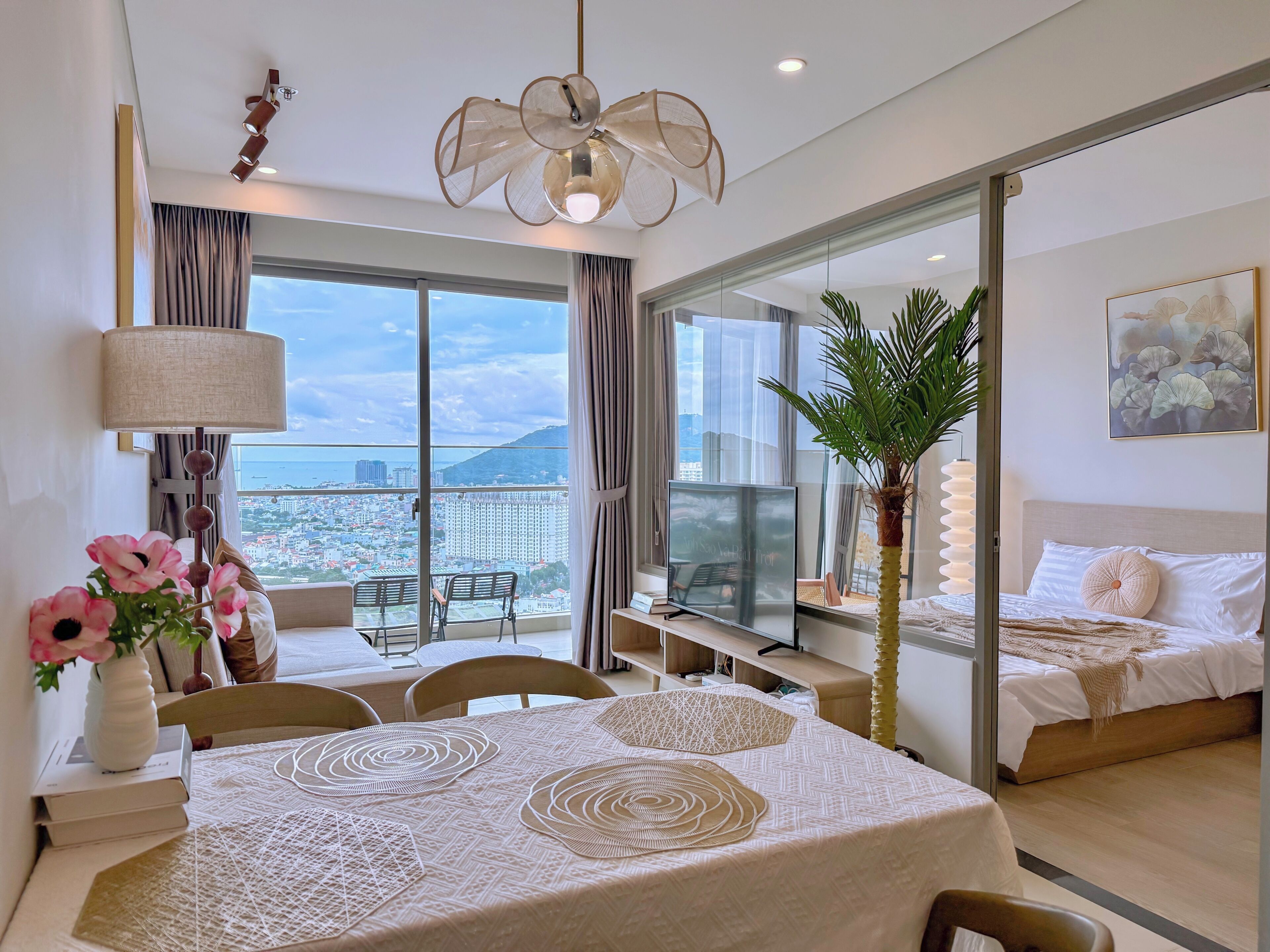 A modern hotel room with a large window, a dining area, a bed, and a desk.