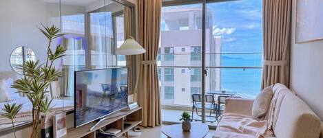 Una sala de estar moderna con un televisor de pantalla plana, un sofá, una mesa de centro y un balcón con vistas al mar.