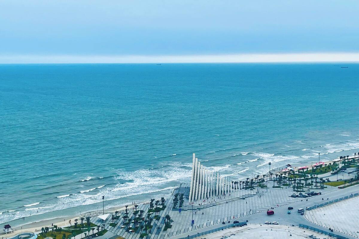 Un passeig marítim amb una zona central per vianants, davant de la platja, i una vista clara del mar.